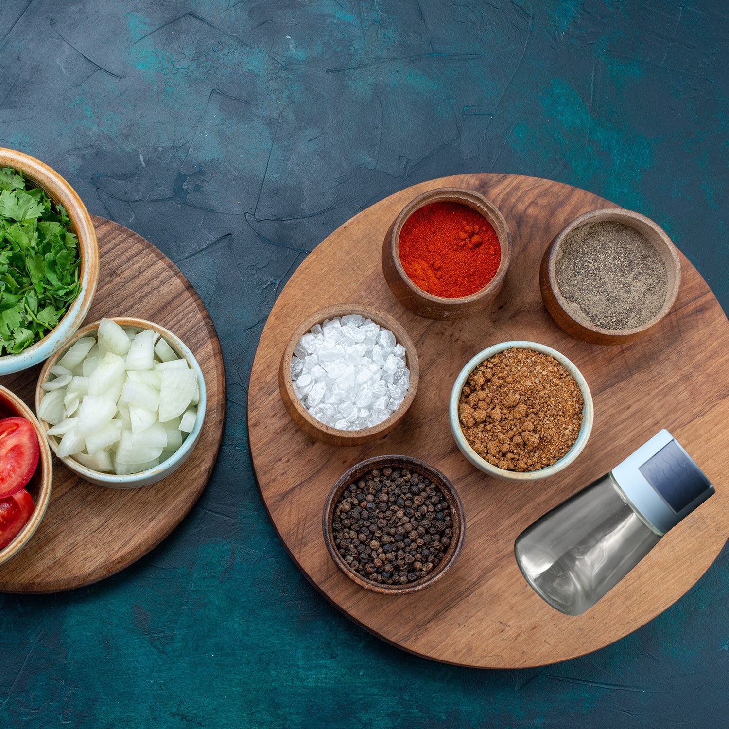 Wukusy glass salt bottle set with stainless steel lid next to spices in wooden bowls on round cutting board