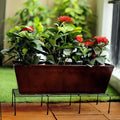 Wukusy metal balcony plant stand holding a rectangular planter with green plants and red flowers