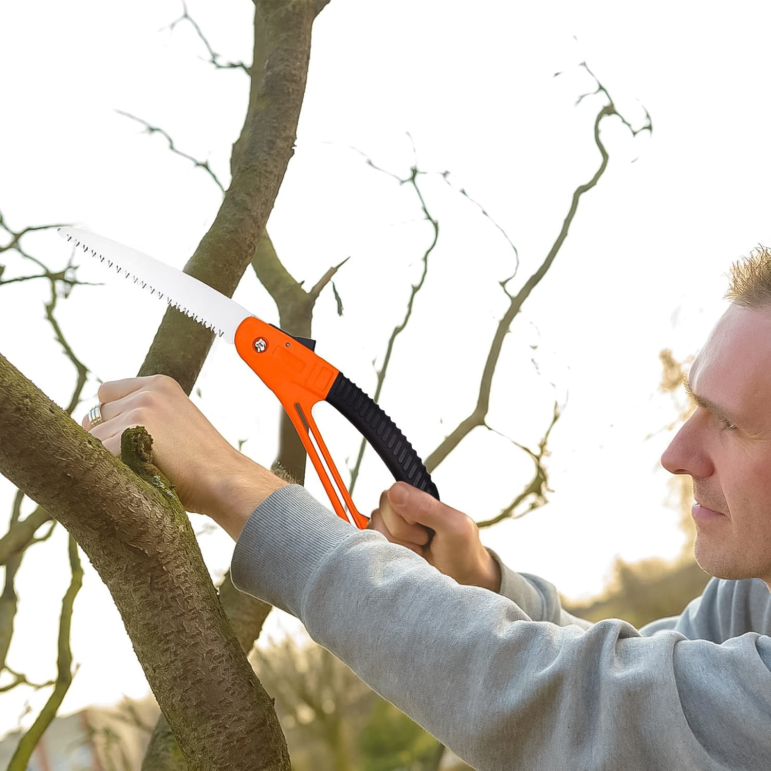 Man using Wukusy mini folding pruning saw with orange handle to cut tree branch in garden