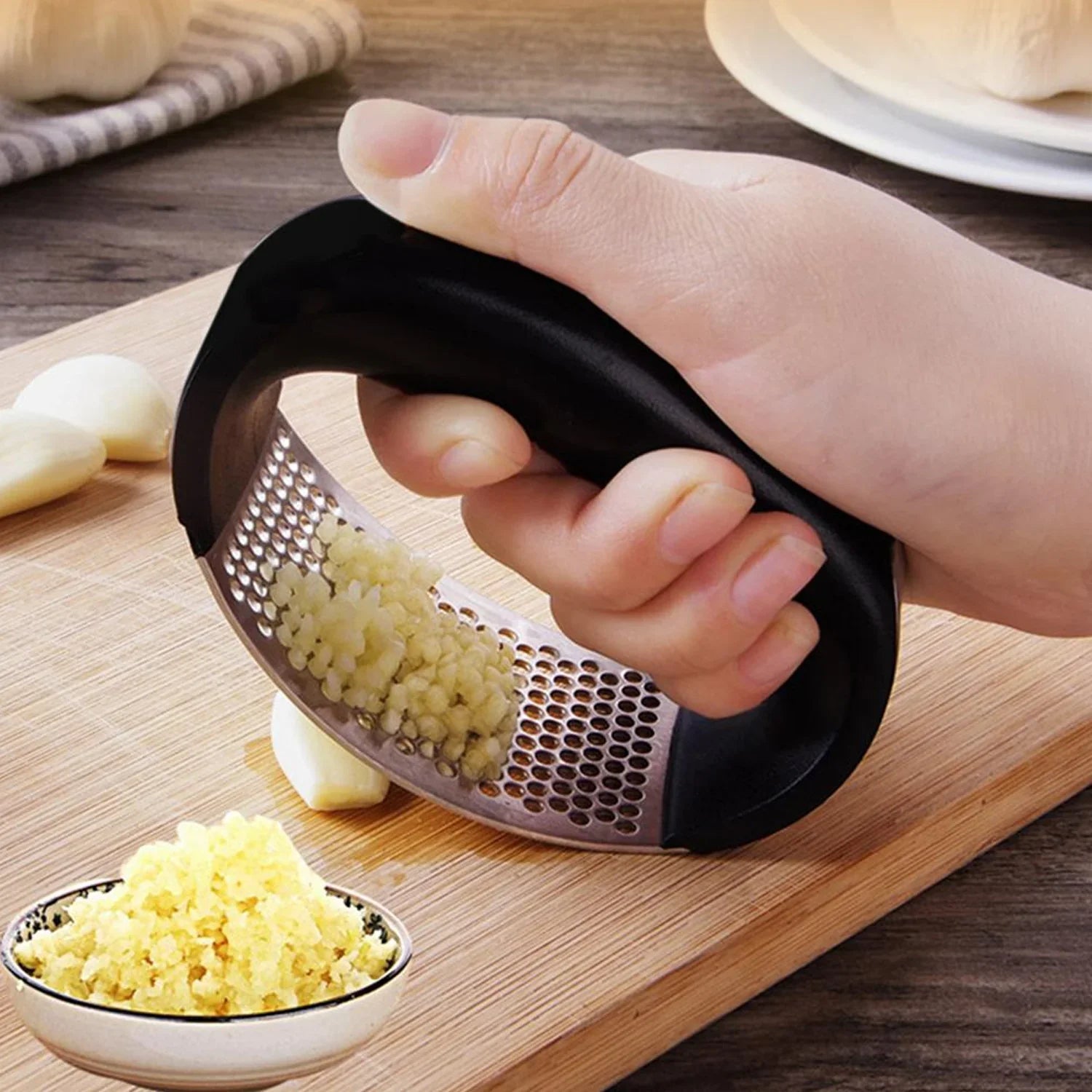 Stainless Steel Garlic Crusher with Ergonomic Handle - Market FindsMarket FindsHand using stainless steel garlic crusher with black handle to mince garlic on wooden cutting board