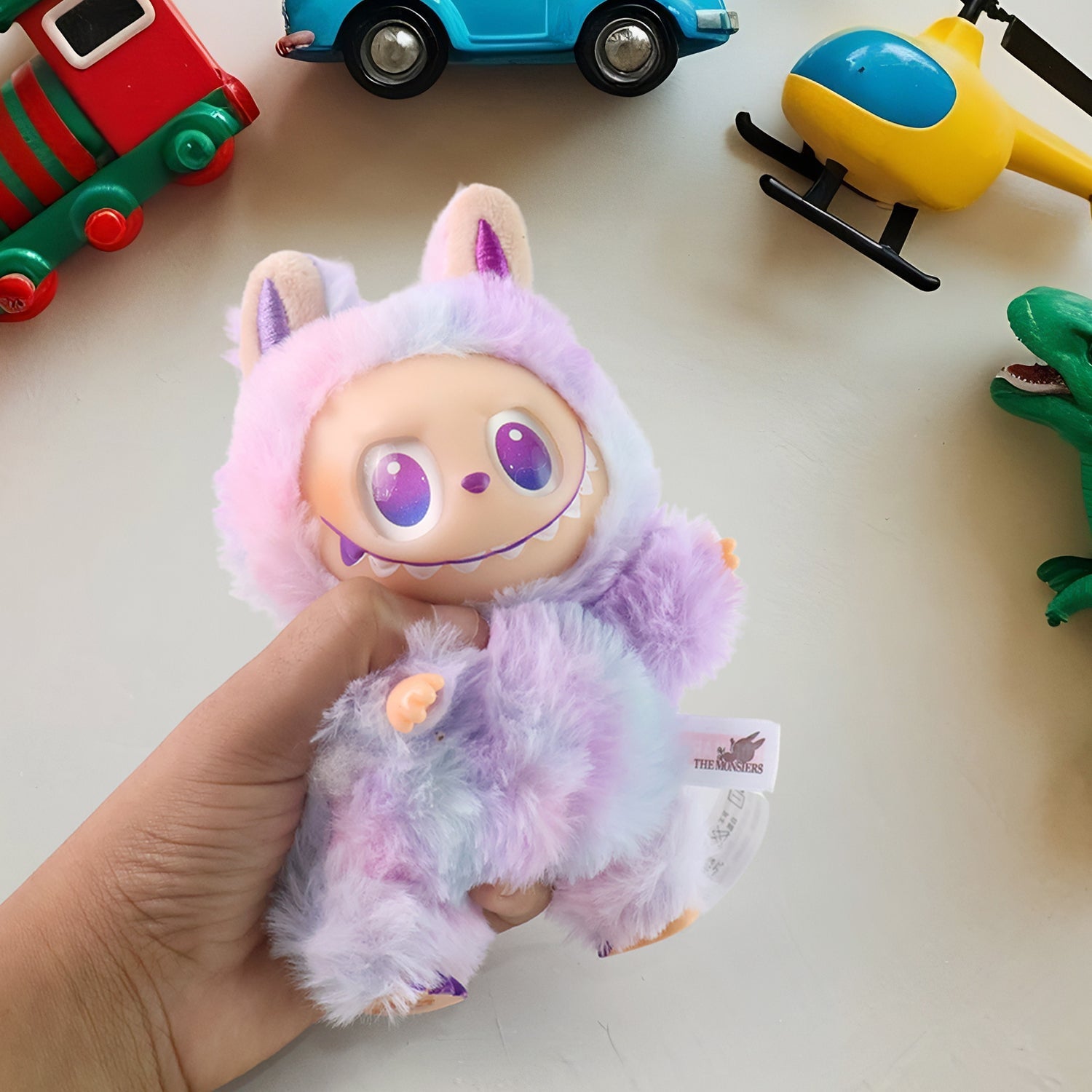 Wukusy light purple plush keychain toy held in hand surrounded by colorful toy vehicles