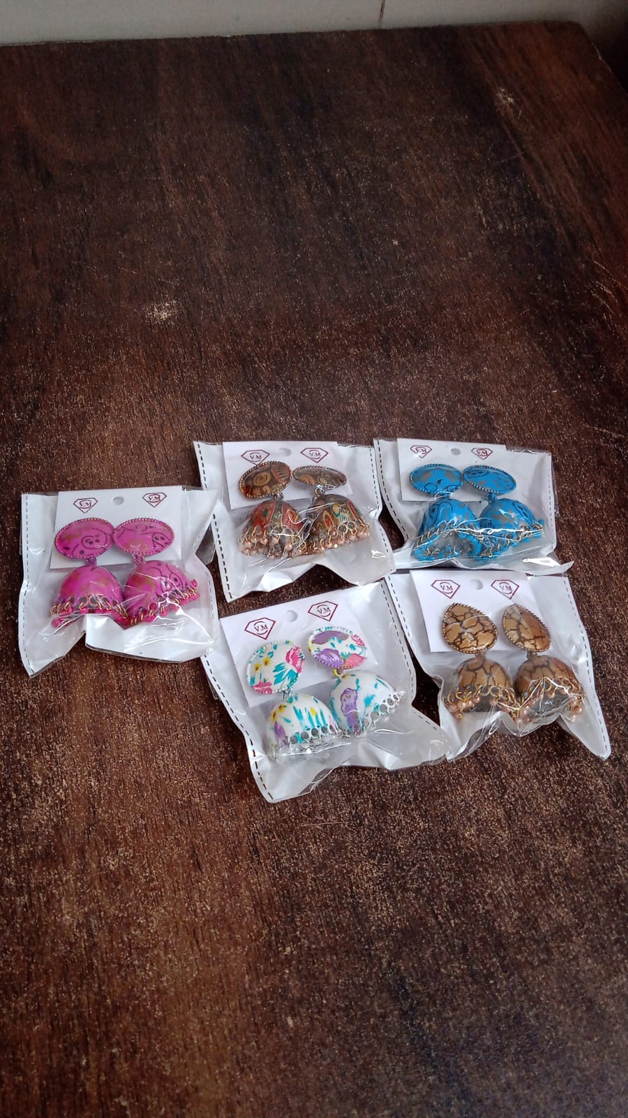 Wukusy traditional jhumka earrings set in various colors including pink, brown, blue, and multicolor on a wooden surface